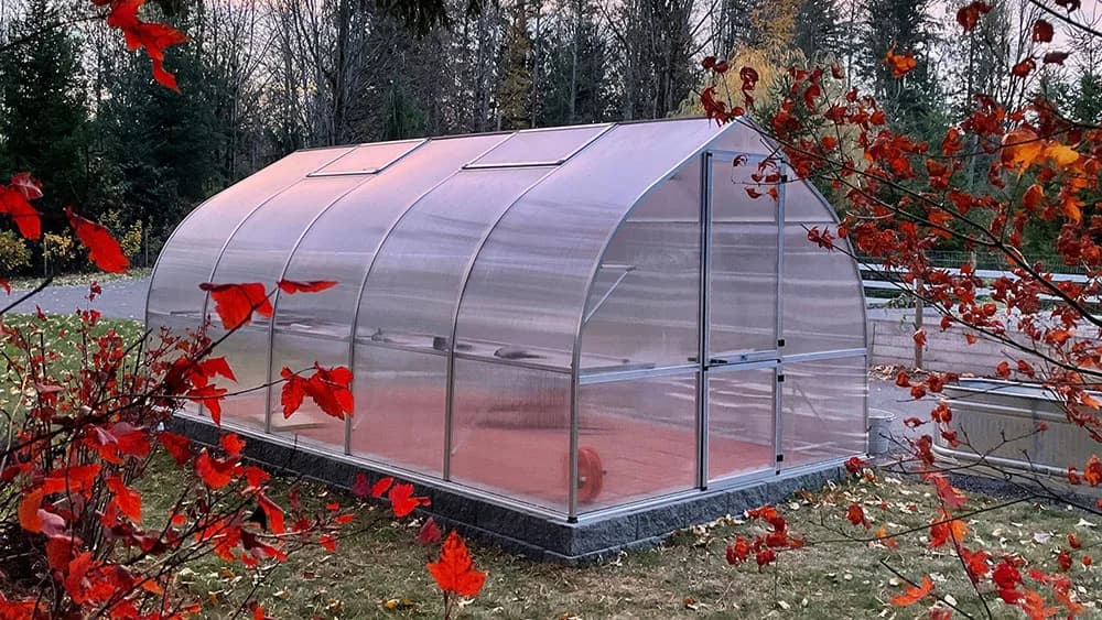 Riga greenhouse on a stone foundation in a fall garden framed by red maple leaves