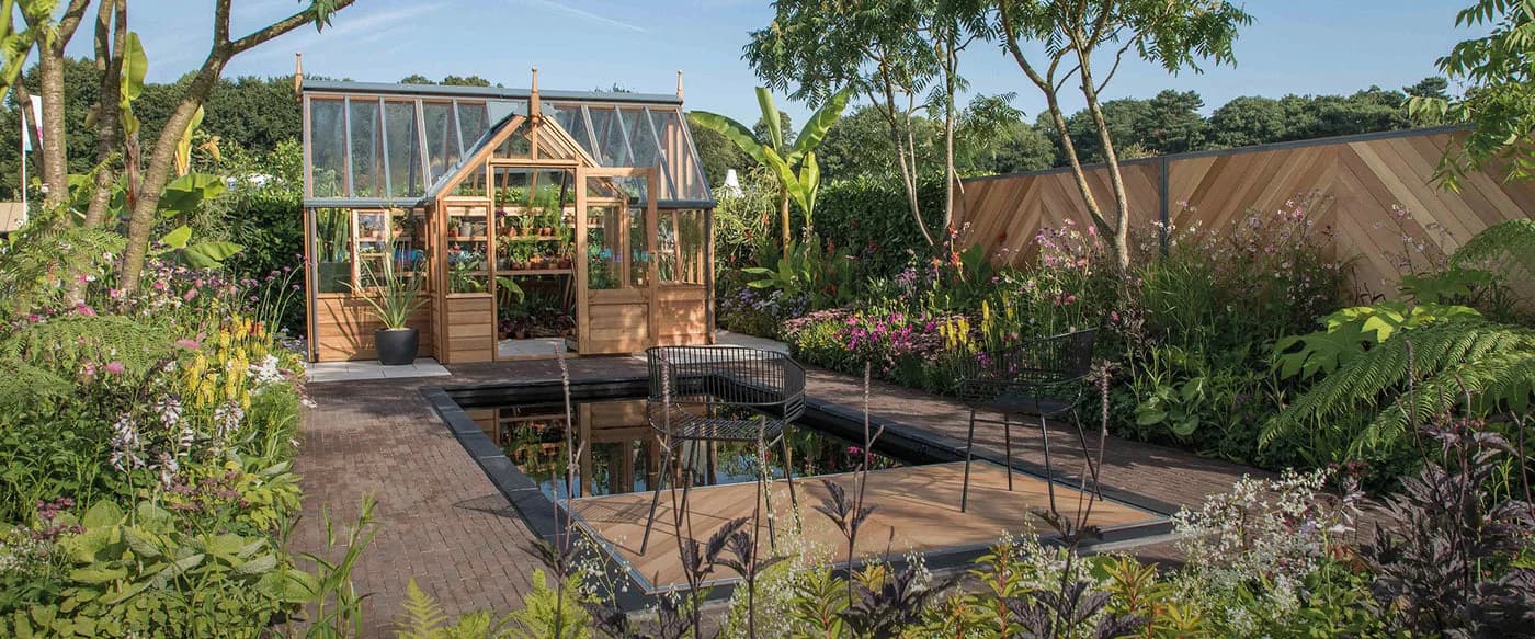 Gabriel Ash RHS Portico cedar greenhouse on display in a show garden with a reflecting pool