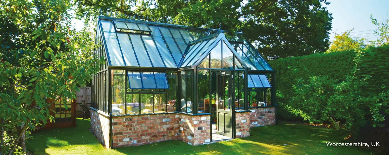 Hartley Botanic Victorian Lodge glasshouse with a porched entrance on a reclaimed-brick dwarf wall in a Worcestershire garden