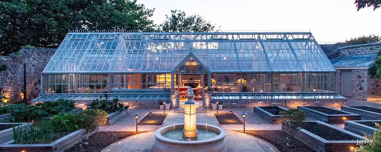 Hartley Botanic Victorian Pavilion glasshouse lit from inside at dusk in a walled kitchen garden on Jersey