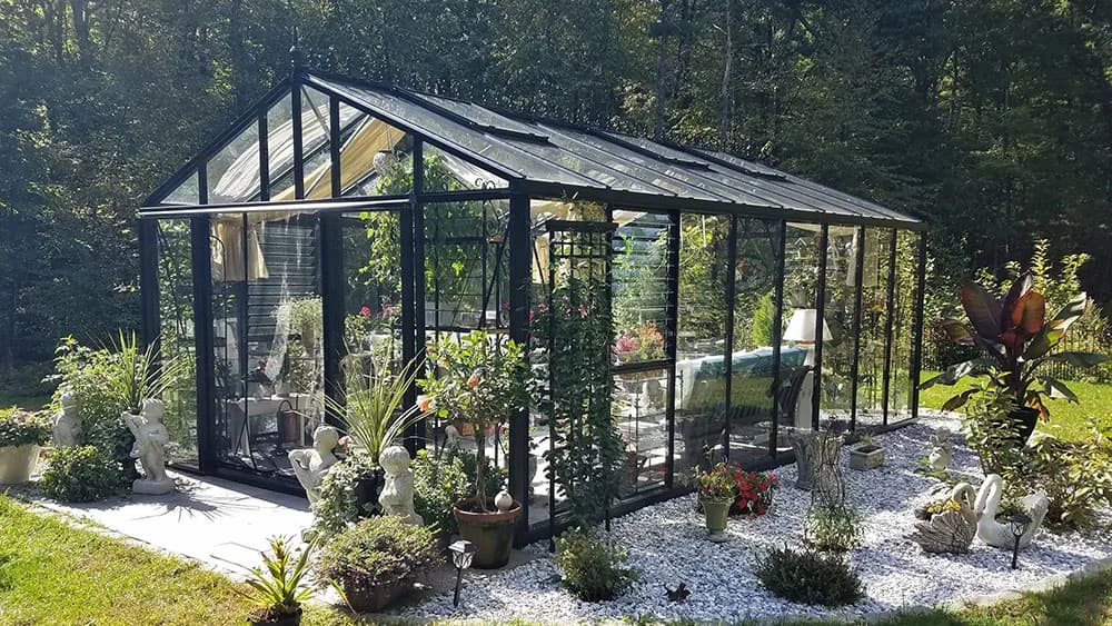 Black Janssens Royal Victorian greenhouse with decorative roof cresting in a wooded backyard