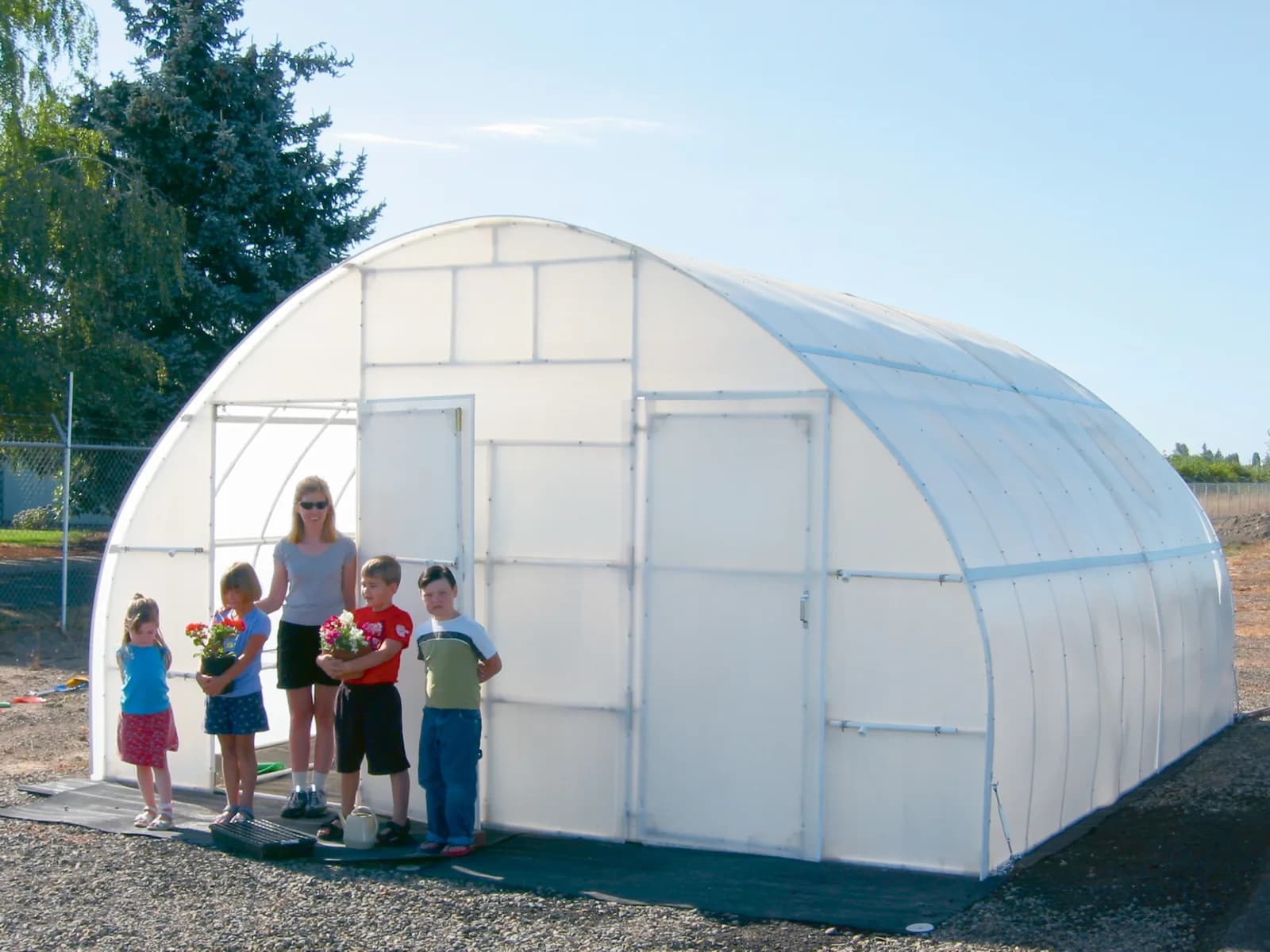 Large Solexx Conservatory greenhouse with a teacher and school children holding potted flowers outside the door